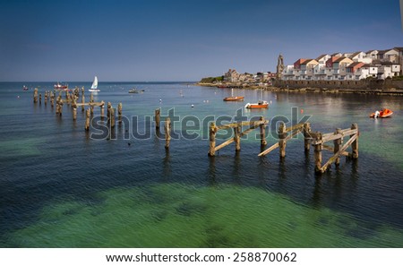 The old pier posts can be seen in the blue-green waters under the new houses perched on the seafront