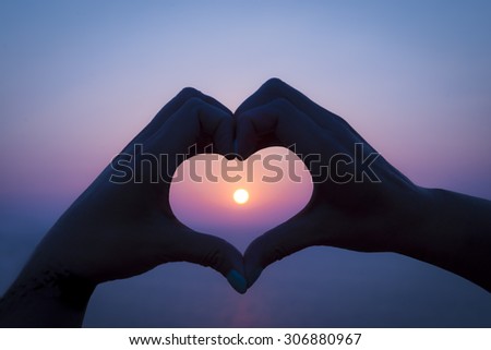 Two hands make a heart around the setting sun on a greek island holiday