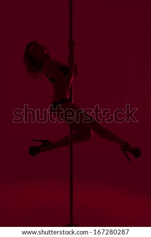 Young beautiful brunette girl doing pole dancing exercise