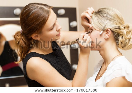 Woman applying make up for a bride in her wedding day near mirror