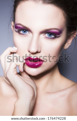 Beautiful brunette woman with creative make up violet eye shadows, blue eyes and full red lips with her hand under her chin