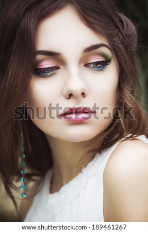Portrait of a beautiful brunette woman in white dress and colorful make up outdoors