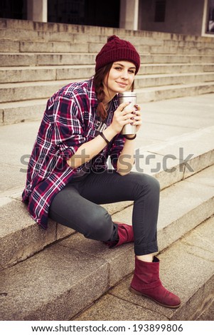 Brunette woman in hipster outfit sitting on steps on the street. Toned image
