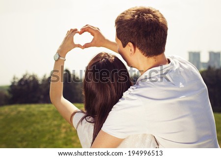 Beautiful couple on a date walking at the park hugging and making heart gesture
