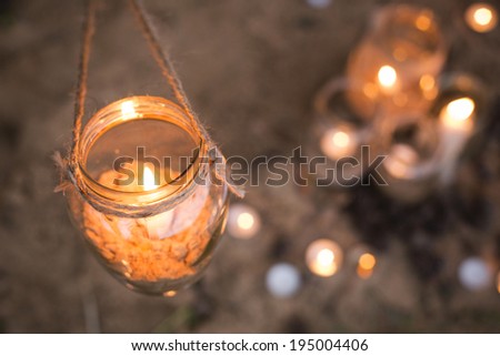 Beautiful decorated romantic place for a date with jars full of candles hanging on tree and standing on a sand. Copy Space