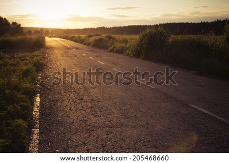 Empty asphalt country road on a sunset with a horizon ahead