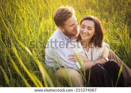 Beautiful hipster couple in love on a date outdoors in park having fun. Bearded red hair man. Brunette woman in black skirt and white blouse. In grass