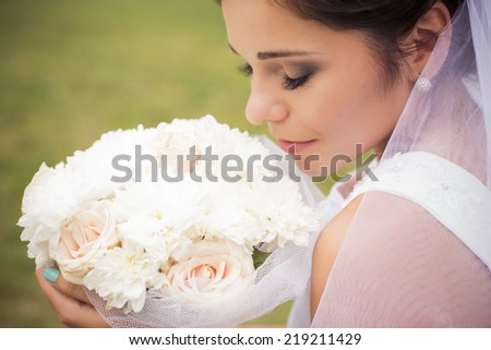 Beautiful bride preparing to get married in white dress and veil with bouquet of roses in the park alone. outdoors. copy space