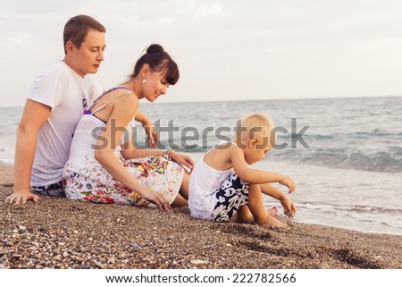 Family sitting on a  sand seashore near sea looking at each other, relaxing on a vacation trip, looking on her husband. copy space