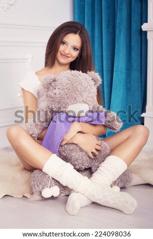 Beautiful brunette woman on a 7th month pregnancy in white underwear with soft bear in hands. light interior.