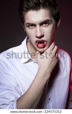 Young sexy man dracula vampire with red eyes and fangs, mouth covered in blood
