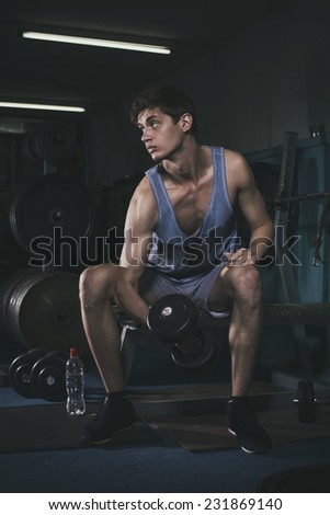 Slim fit man trains in gym lifting dumbbell. alone. one. indoors