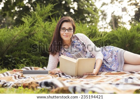 Beautiful brunette senior woman studying for her exams sitting on a plaid reading book in a dress. Outdoors. Copy Space