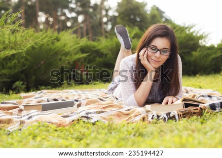 Beautiful brunette senior woman studying for her exams sitting on a plaid reading book in a dress. Outdoors. Copy Space