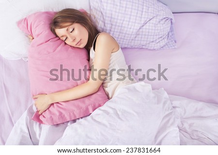 Beautiful blonde woman sleeping in her bed in pajamas, smiling, hugging pillow