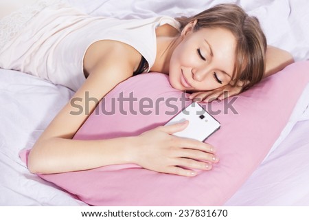 Beautiful blonde woman sleeping with a phone in her hand, waiting for a call, in her bed in pajamas, smiling