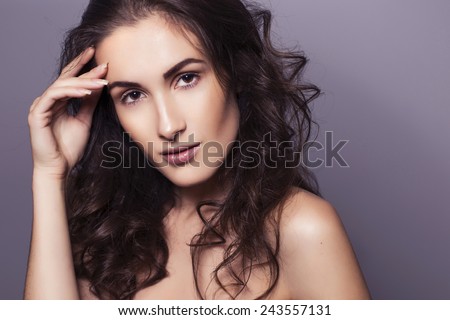 Beautiful brunette woman with clear fresh skin and curly hair on a dark background, hand on face. toned image. copy space