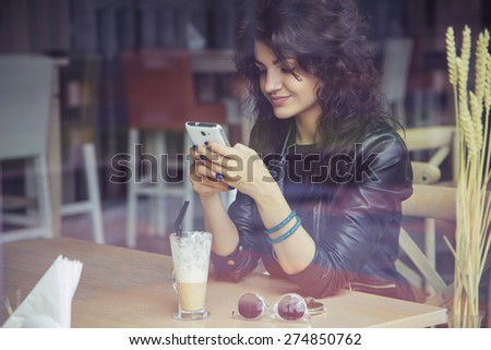 Brunette beautiful stylish caucasian woman in casual outfit on a walk on european city street sitting at the cafe typing message on her phone. copy space