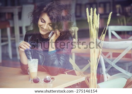 Brunette beautiful stylish caucasian woman in casual outfit on a walk on european city street sitting at the cafe talking on her phone. copy space