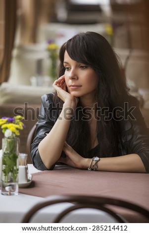 Brunette beautiful stylish caucasian woman in casual outfit on a walk on european city street sitting at the cafe waiting