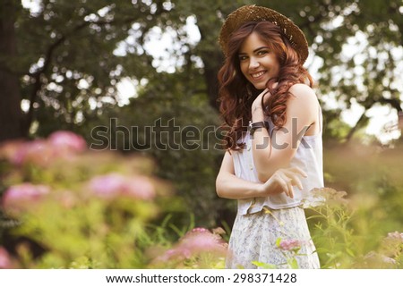 Young beautiful caucasian white brunette woman with curly hairstyle and make up, in a summer outfit: dress and a hat in park. outdoors