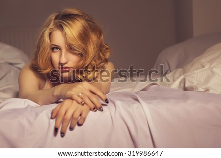 Beautiful blonde fit woman with make up and curly short hairstyle laying on bed in underwear in sensual sexy poses. copy space