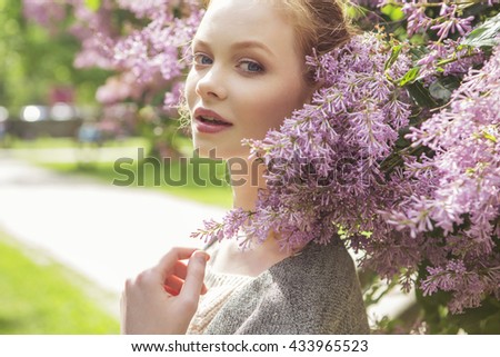 Beautiful red hair ginger slim young woman with fresh skin in casual outfit, posing with flowers. Sunny summer day in park (nature). Daylight
