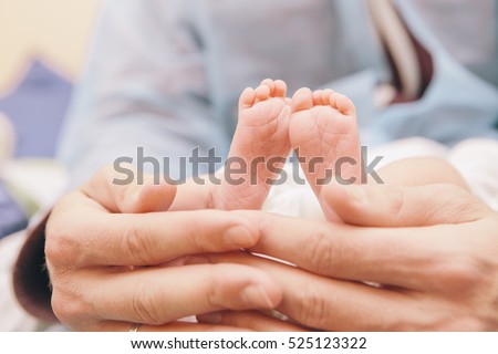 Little infant newborn child in maternity hospital on his fathers arms. Man holding sleeping baby\'s feet. Lifestyle