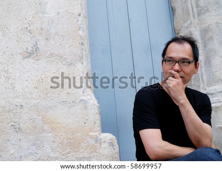 outdoor portrait of a young asiatic man thinking  and looking ahead against an antic blue door for background
