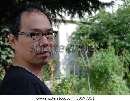 outdoor portrait of a young asiatic man thinking  and looking ahead against garden for background