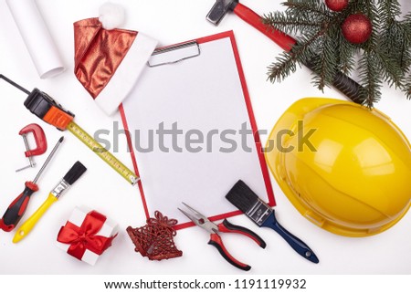 Construction hard hat, tools, blank clipboard, gifts, fir tree branches and Christmas decoration on a white background. Top view with copy spase. New Year and Christmas. Construction concept.