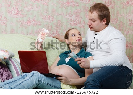 The young pregnant woman with her husband, sitting on sofa at home, plan the family budget.
