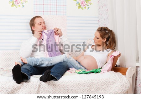 Happy pregnant family  with children's clothes sit on the bed at home.