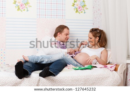 Happy pregnant family  with children\'s clothes sit on the bed at home.