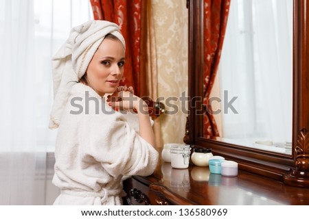 Young woman with cosmetic cream sits before a house  dressing table. Concept body care.
