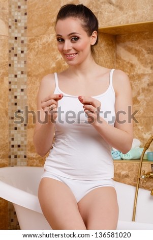 Happy young woman checking pregnancy test sits in a bathroom. Positive result.