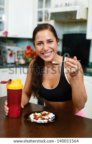 The sports young woman with a protein cocktail in a shaker and plate with nutritional supplements  sits in house kitchen. Sports nutrition.