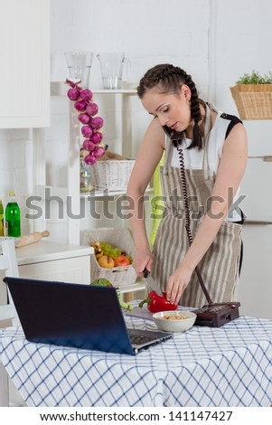 Beautiful woman in an apron with notebook and phone cooks in the kitchen.