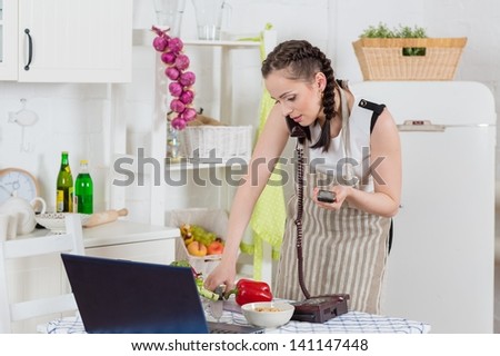 Stressed  young woman in an apron with notebook and phone cooks in the kitchen.