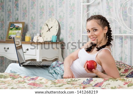 Young woman with laptop sits on the house bed in the bedroom.