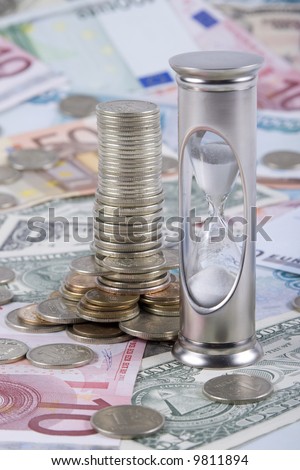 Hourglass and tower from the coins, standing on a floor from banknotes. Concept for time is money.