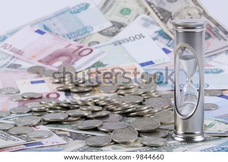 Hourglass and  coins, standing on a floor from banknotes. Concept for time is money.