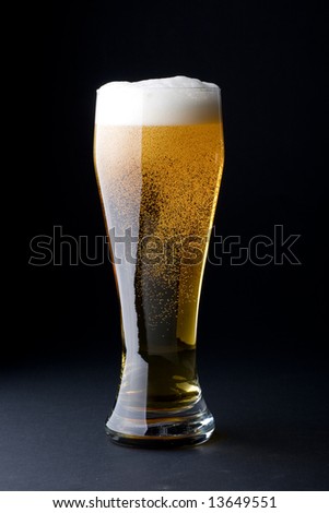Fresh foamy beer in a glass on a black background.