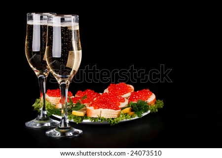 Sandwiches with red caviar and two glasses of champagne on a black background