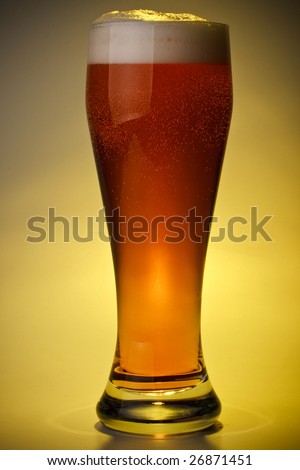 Glass of fresh foamy beer on a yellow background