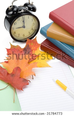Pile of books, writing-book, pen, alarm clock and autumn leaves on a white background. Concept for \