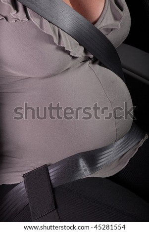 The pregnant woman fastened by a seat belt sits in the car.