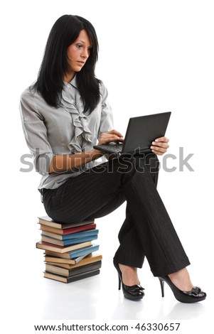 The attractive student sits on a pile of books with the laptop on a white background.