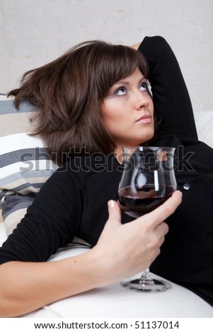 Young woman relaxes at home on the white sofa with a glass of red wine