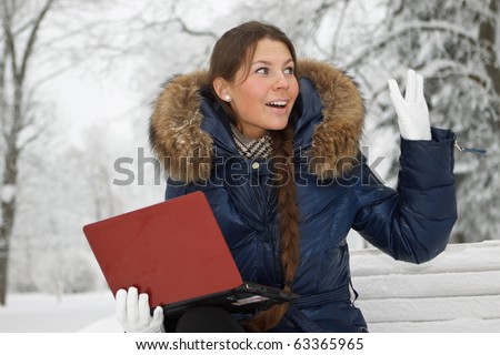 The beautiful girl with the laptop sits on a bench in winter park.